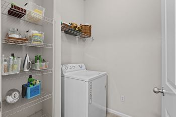 A full size washing machine inside a laundry room, with several wire rack shelves for storage.